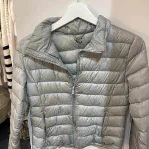 Grå superlätt dunjacka - Säljer en grå superlätt dunjacka i storlek 158, perfekt för kyliga dagar. Jackan har en dragkedja framtill och är quiltad för extra värme. Den är i mycket bra skick och passar både höst och vår. En stilren och praktisk jacka för alla tillfällen!