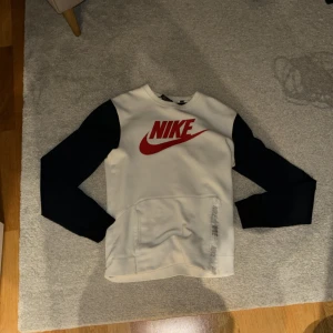 Vit och Blå Nike tröja - Säljer en snygg vit och mörkblå Nike tröja i storlek XS. Jag bär sorlek S och den passar även mig som bär S.  Perfekt för en sportig look eller bara för att chilla. Tröjan har en dragkedja vid fickan (se bild) på sidan för extra stil och funktionalitet. Passar perfekt till både vardag och träning! Fråga gärna efter fler bilder vid intresse 😁