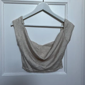 Beige croppad topp - Säljer en snygg beige croppad topp med breda axelband och en draperad framsida. Perfekt för sommardagar eller en utekväll. Toppen är i ett mjukt material och har en stilren design som passar till det mesta. Ett måste i garderoben!