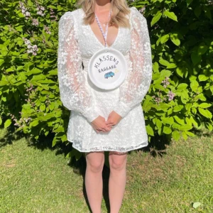 Student klänning spetsklänning med puffärmar  - Intresse koll på en superfin vit spetsklänning med v-ringning och långa puffärmar. Perfekt för  studentfirande! Klänningen har en kort längd och ett vackert blommigt mönster. Den är i mycket bra skick. Passar perfekt för dig som vill sticka ut med stil! Finns inte längre att köpa 