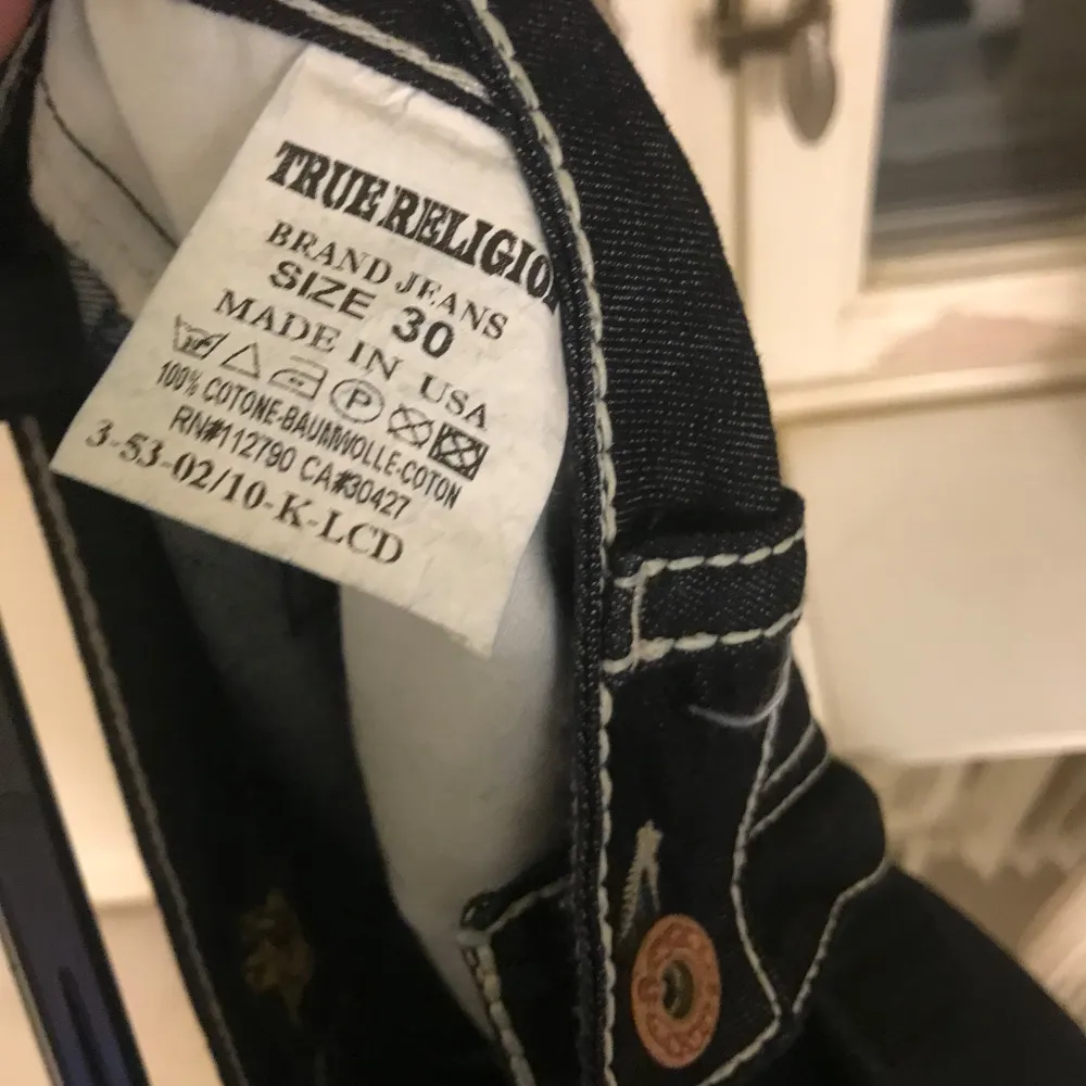 Säljer ett par snygga mörkblå jeans från True Religion i storlek 30. De har vita kontrastsömmar och klassiska femficksdesign. Jeansen är tillverkade i USA av 100% bomull och har en bekväm passform. Perfekta för både vardag och fest!. Jeans & Byxor.