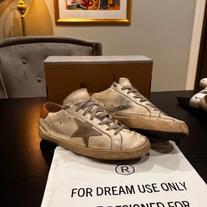 Golden Goose sneakers i beige och brun - Säljer ett par Golden Goose sneakers i vit- beige med bruna detaljer. Sliten look. Perfekta för en avslappnad stil och passar till nästan allt! Fråga på!