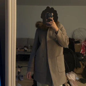 Beige kappa med pälskrage - Säljer en snygg beige kappa med en mysig pälskrage. Perfekt för höst och vinter! Den har långa ärmar och stora fickor framtill. Storlek S/M 