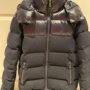 Svart pufferjacka från Polo Ralph Lauren - Säljer en snygg svart pufferjacka från Polo Ralph Lauren. Jackan har en quiltad design med dragkedja och en broderad logga på bröstet. Perfekt för kyliga dagar med sin varma och stiliga look. Den har en huva och är i mycket bra skick. Passar perfekt för höst och vinter!
