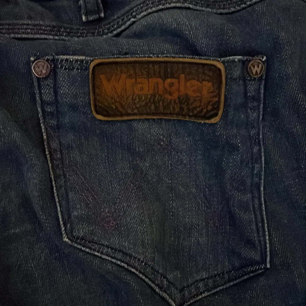 W27 L32 Säljer ett par klassiska blå jeans från Wrangler. De har en snygg, sliten look och är i bra skick. Perfekta för vardagsbruk med en straight passform. Märkesloggan syns tydligt på bakfickan. Passar till alla tillfällen, både avslappnade och lite mer uppklädda. . Jeans & Byxor.