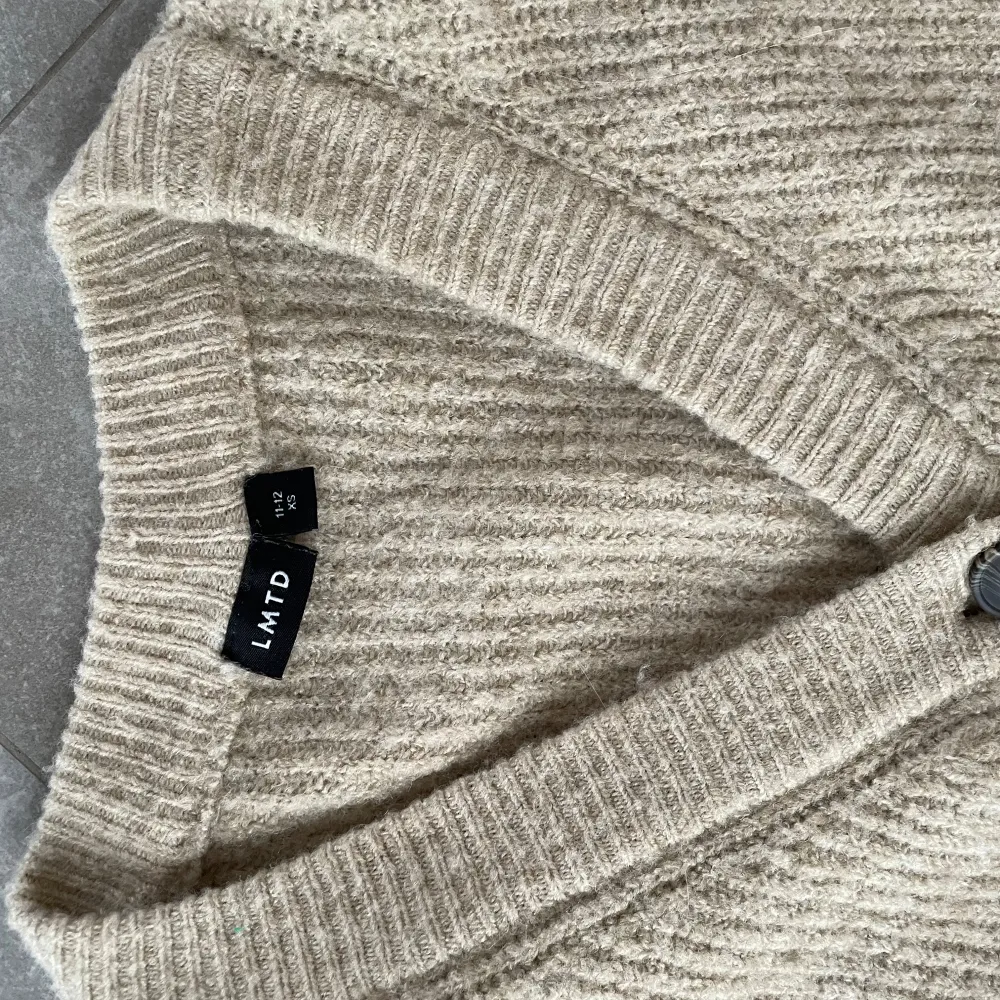 Säljer en mysig beige stickad kofta från LMTD. Koftan har en v-ringad design med knappar framtill och långa ärmar. Perfekt för kyligare dagar och lätt att matcha med olika outfits.. Neuletakit & Villapaidat.