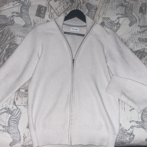 Vit stickad tröja från East West - Säljer en stilren vit stickad tröja från East West. Tröjan har en dragkedja framtill och långa ärmar, perfekt för kyligare dagar. Den är i storlek S och passar bra till både vardag och mer avslappnade tillfällen. Den är s men sitter lite mindre , köpt för 900kr