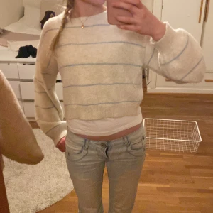 Beige randig stickad tröja - Säljer en snygg och mysig beige stickad tröja med blå ränder. Tröjan är croppad och har långa ärmar med ribbade muddar. Super mjuk och skön! Köp snabbt och enkelt via ’köp nu’!💞