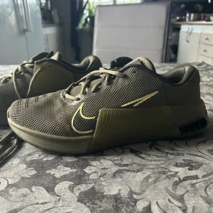 Olivgröna Nike träningsskor - Snygga olivgröna Nike träningsskor med snörning. Skorna har en diskret Nike-logga på sidan och är perfekta för träning. De har en modern design med meshmaterial för bra andningsförmåga. Som det syns på bild 4 är det liten defekt på sulan, men inget som man lägger märke till.