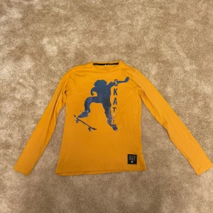 Gul långärmad tröja från Name It - Passar åldrar 13-14 år.Gul långärmad tröja med ett tryck av en skateboardåkare och ordet 'SKATE' skrivet vertikalt. Trycket är i en mörkare blå nyans. Tröjan har en rund halsringning.    Storlek: 158-164 skick: 7/10  Din stil: spara inlägget så du inte missar denna kappa Inte din stil: Kolla min profil. Du kommer hitta något för alla kön och åldrar.