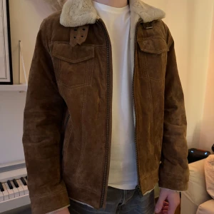 Brun mockajacka från Jofama - Säljer en snygg brun mockajacka från Jofama med en mysig pälsfodrad krage. Jackan har dragkedja framtill och två bröstfickor med lock. Perfekt för kyligare dagar och ger en stilren look. Nypris 3999kr
