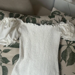 Vit klänning med puffärmar - Säljer en söt vit klänning med smockdetaljer och puffiga kortärmar. Perfekt för sommarens alla tillfällen. Klänningen har en åtsittande passform och är gjord i ett lätt och bekvämt material. Endast använd 1 gång sedan bara hängt i klädkammaren.😊