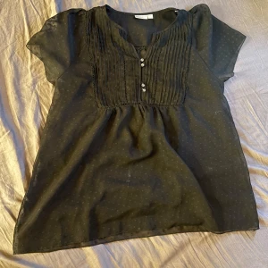 Svart blus från Lindex - Säljer en svart blus från Lindex med korta ärmar och dekorativa knappar framtill. Blusen är ganska genomskinlig men jag brukar ha ett linne under💕den är i storlek 44 men sitter bra på mej som är xs-m💕skriv om du vill ha fler bilder💕