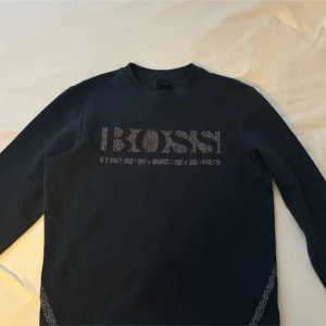 Svart tröja från Boss - Säljer en stilren svart tröja från Boss med långärmad design. Tröjan har ett diskret mönster med Boss-loggan på framsidan. Perfekt för en avslappnad men ändå snygg look.