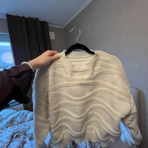 Vit stickad tröja - Säljer en mysig vit stickad tröja med vågigt mönster. Tröjan har långa ärmar och en rund halsringning. Perfekt för kyligare dagar och ger en avslappnad look. Står igen storlek eller märke, tror den är i M/S/XS