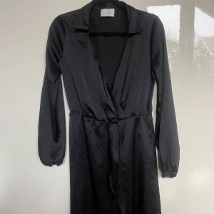 Svart omlottklänning från Neo Noir - Snygg svart omlottklänning från Neo Noir med långa ärmar. Storleken står inte men skulle säga 38