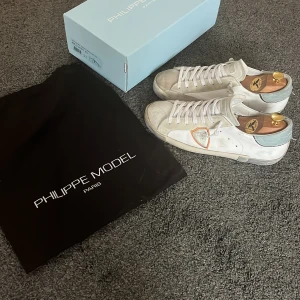 Vita Phillipe model skor - Säljer dessa vit, blå, oranga Phillipe model skor då jag köpt andra. De är i helt okej skick, lite skador på hälen, men lagade med skyddslappar, lite skador på mockan som man ser på bilden och där fram på sulan finns det lite slitningar. Men annars snygga skor!