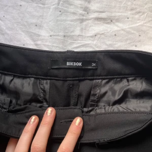 Svarta byxor från BikBok - Snygga svarta byxor från BikBok i storlek 34. De har en klassisk design med dragkedja och knapp framtill. Perfekta för en stilren look. Lågmidjade 🫶🏼