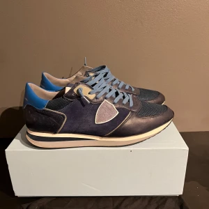 Blå sneakers från Philippe Model - Snygga blå sneakers från Philippe Model med ljusblå snörning och detaljer i beige. Skorna har en stilren design med en mix av material som ger en modern look. Perfekta för en avslappnad stil.