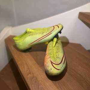 Nike mercurial  - Säljer ett par gula fotbollsskor från Nike med snörning och en iögonfallande design. Skorna har en grön och orange toning med svarta detaljer på sulan. Perfekta för fotbollsplanen med sin lätta och smidiga konstruktion.