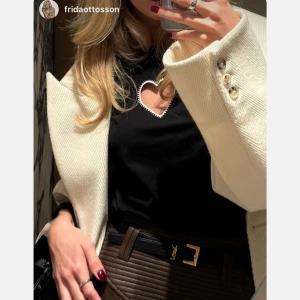 Svart t-shirt med hjärtformad detalj från Cloeys - Snygg svart t-shirt från Cloeys med en unik hjärtformad detalj framtill. Perfekt för en stilren look med en twist. T-shirten har korta ärmar och en normal passform. Helt ny i paketet fortfarande! Strlk M