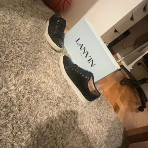 Svarta sneakers från Lanvin - Snygga svarta sneakers från Lanvin med vit sula och snörning. Perfekta för en stilren look. Skorna har en klassisk design som passar till många olika outfits.