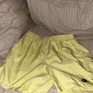 Gula shorts från Nike - Snygga gula shorts från Nike med elastisk midja och en liten ficka bak. Perfekta för sommarens alla aktiviteter. De har en avslappnad passform och är gjorda i ett lätt material som känns skönt mot huden.