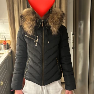 Svart dunjacka med pälsdetaljer - Snygg svart dunjacka från hollies. Jackan har en figurnära passform storlek 36. Avändskick❤️Pris går alltid att diskuteras!