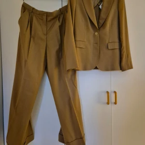 Brun kostym från By Malene Birger - Elegant brun kostym från By Malene Birger. Overzise. Kavajen har en klassisk design med en knapp och fickor framtill. Byxorna har en stilren passform med pressveck och uppvikta benslut. Perfekt för en stilfull look. Något litet slitet nertill på byxorna, annars bra vintage skick. Själv köpt kostymen i secondhand butik för 1299:- men var tyvärr för stor för mig. 🤎