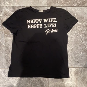 Svart t-shirt - Snygg svart t-shirt från Ge-kås med texten 'Happy Wife, Happy Life!' i vitt. Perfekt för en avslappnad stil. T-shirten har en klassisk passform och korta ärmar.