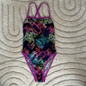 Färgglad baddräkt från Speedo - Säljer en cool baddräkt från Speedo med neonfärger och grafiskt mönster. Den har smala axelband som korsas i ryggen och en öppen ryggdesign. Perfekt för simträning eller strandhäng!