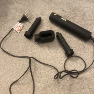 Svart hårstyler med utbytbara tillbehör - Säljer en svart hårstyler med flera utbytbara tillbehör för olika stylingalternativ. Den har  guldiga detaljer på handtaget. Perfekt för att skapa olika frisyrer hemma.