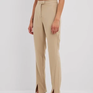 Beige kostymbyxor med slits - Snygga beige kostymbyxor med hög midja och slits vid bensluten. Perfekta för en stilren look. Byxorna har en rak passform och stängs med dragkedja och knapp framtill.