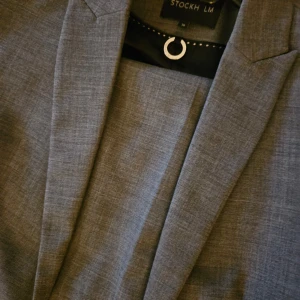 Grå kavaj från Stockh LM - Tvådelad damkostym. Snygg grå kavaj från Stockh LM modell Karen  i damstorlek M. Perfekt för både formella och semi-formella tillfällen. Kavajen har en klassisk passform med två knappar och fickor fram. Materialet känns bekvämt och ser stilrent ut. Passar utmärkt till höst och vår. Kavaj stl 36, byxor stl 40.