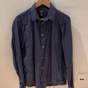 Mörkblå skjorta från H&M - 52% linen, 48% cotton. Säljer en snygg mörkblå skjorta från H&M i storlek M. Skjortan har en klassisk krage och knappar hela vägen ner. Den är långärmad och passar perfekt för både vardag och fest. Materialet känns bekvämt och är lätt att matcha med olika outfits. Perfekt för höst och vår!