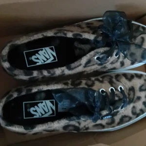 Leopardmönstrade fursneakers vans - Säljer ett par coola Vans sneakers i leopardmönster. De har en snygg rosett i svart spets och klassisk snörning. Perfekta för att ge din outfit en extra edge! 🐆