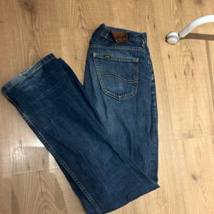 Blå jeans från Lee - Säljer ett par klassiska blå jeans från Lee i mycket bra skick. De har en normal passform och är perfekta för vardagsbruk. Jeansen har en traditionell femficksdesign och en knappgylf. Perfekta för både höst och vår!