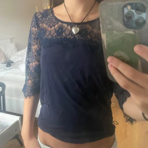 Mörkblå spetsblus - Säljer en elegant mörkblå blus med spetsdetaljer. Blusen har trekvartsärmar och en vacker spetsdesign över axlar och ärmar. Perfekt för både vardag och festliga tillfällen. Passar bra till både jeans och kjol!