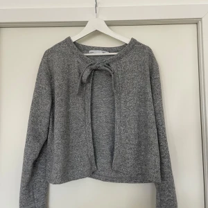 Grå kofta - En grå kofta ifrån Laget 157 i storlek M. Koftan passar till alla tillfällen och är perfekt nu när de börjar bli kallare ute.Koftan är grå och har två band fram till som man kan knyta till en rosett som på bilden eller bara ha hängandes som dem är. 