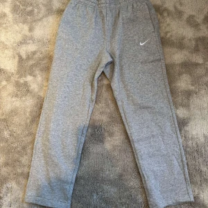 Grå mjukisbyxor från Nike - Säljer ett par grå mjukisbyxor från Nike i nytt skick. De har en elastisk midja och en liten Nike-logga på benet. Perfekta för en avslappnad dag hemma eller lätt träning. Superbekväma och stilrena!