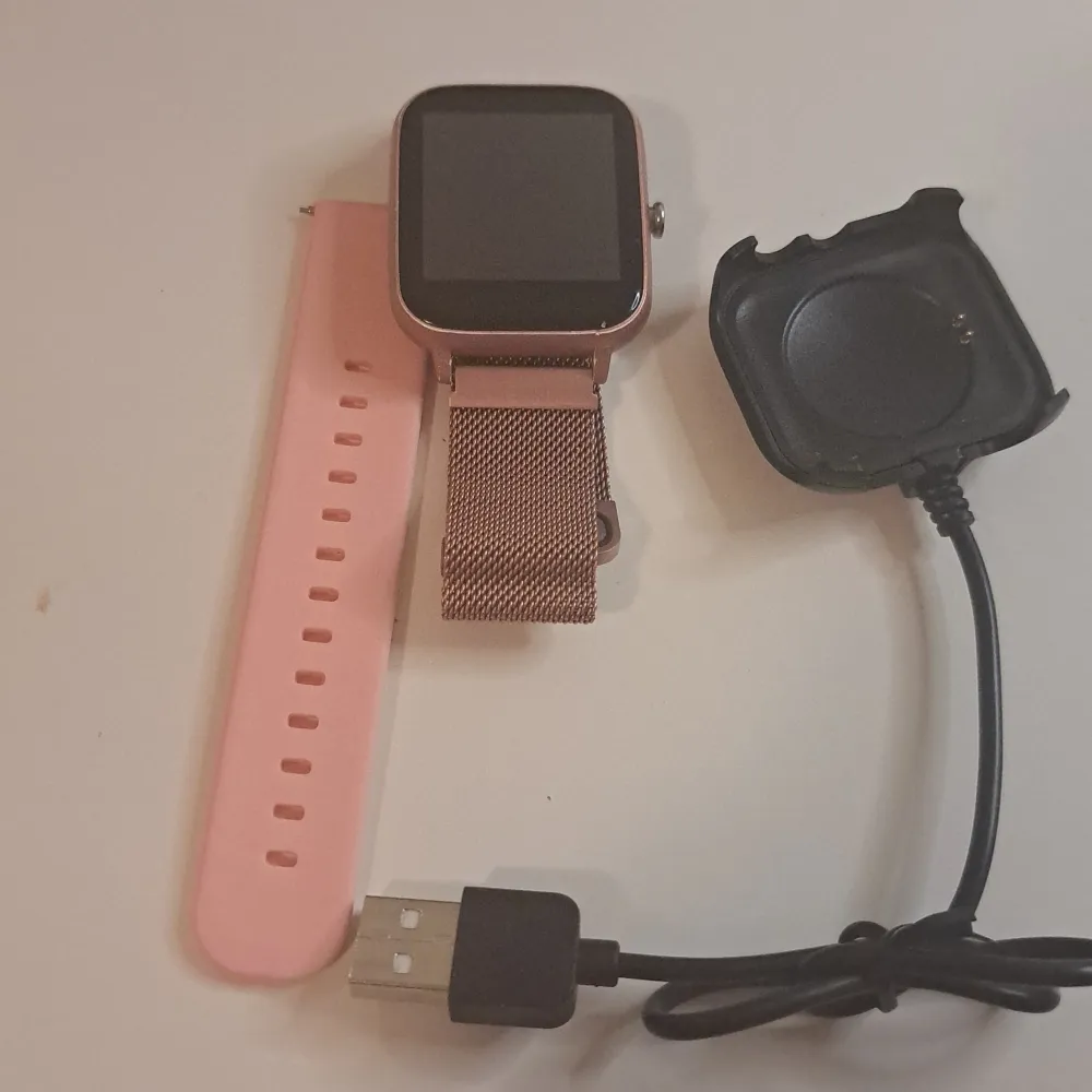 Säljer en snygg smartklocka med ett stilrent rosa mesh-armband och en extra rosa silikonrem. Klockan har en fyrkantig skärm och kommer med en laddare. Perfekt för både vardag och träning!. Accessoarer.