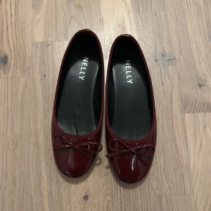 Vinröda ballerinaskor från Nelly - Säljer ett par snygga vinröda ballerinaskor från Nelly i lackat material. De har en söt rosett på tån och är perfekta för både vardag och fest. Skorna är i bra skick och har en klassisk design som passar till det mesta. Perfekta för höst och vår!