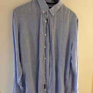 Blå linneskjorta - Säljer en snygg blå linneskjorta från Robbie Moor i herrstorlek. Skjortan har en klassisk krage och knappar hela vägen ner. Perfekt för vår och sommar, och funkar både till vardags och fest. Den är långärmad och har en avslappnad passform. Skjortan är i bra skick och redo för nya äventyr! Köpt för 1000kr.