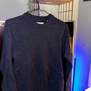 Mörkblå stickad tröja från Jack & Jones - Säljer en snygg mörkblå stickad tröja från Jack & Jones. Perfekt för kyliga dagar med sin mjuka och varma känsla. Tröjan har en klassisk rund hals och långa ärmar, vilket gör den idealisk för både vardag och lite finare tillfällen. Passar perfekt till jeans eller chinos!