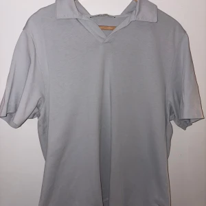 Ljusblå kortärmad piké  - Säljer en stilren ljusblå piké med korta ärmar och en v-ringad krage. Materialet känns mjukt och bekvämt, köpt för 800kr från A day’s march.