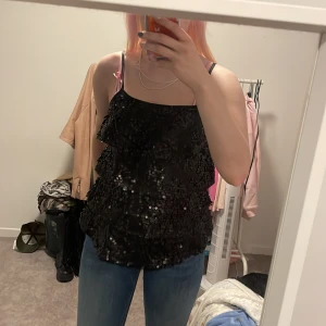 Svart paljettlinne från H&M - Säljer ett snyggt svart linne från H&M, perfekt för fest! Det är täckt med glittriga paljetter och har tunna axelband. Linnet är i storlek XS och ger en glammig look till vilken outfit som helst. Passar perfekt till en utekväll eller speciella tillfällen. ✨