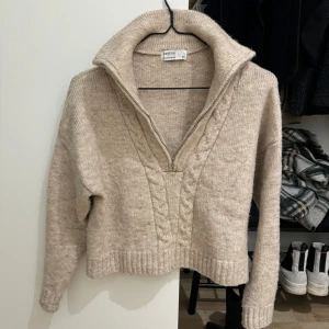 Beige stickad tröja från H&M - Mysig beige stickad tröja från Bershka med en snygg krage och dragkedja framtill. Perfekt för kyliga dagar med sitt varma material och stilrena design. 