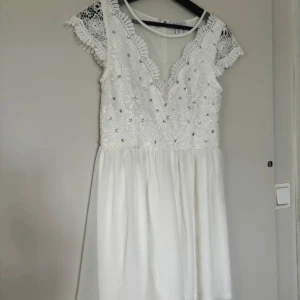 Vit spetsklänning med pärlor - Säljer en superfin vit klänning med spetsdetaljer och pärlor. Den har korta ärmar och en dragkedja i ryggen. Perfekt för sommarens fester eller studentfirande! 💫