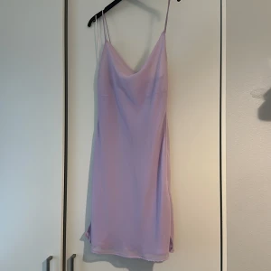 Ljuslila axelbandslös klänning - Säljer en superfin ljuslila klänning med smala axelband. Perfekt för sommarens fester eller en mysig vårdag. Klänningen är i ett mjukt och lätt material som faller snyggt. Den är axelbandslös och har en enkel men elegant design. Aldrig använd innan. Köpt. Från BERSHKA. Storlek M men sitter snarare som S