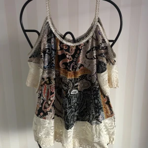 Mönstrad ärmlös topp med spetsdetaljer - Säljer en unik ärmlös topp med ett färgglatt paisleymönster och vackra spetsdetaljer. Toppen har en luftig passform och tunna axelband, perfekt för sommardagar. Den är tillverkad i Italien och har en bohemisk stil som passar både till vardags och fest.